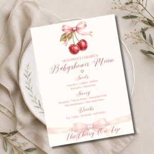Op de afbeelding: Een witte rechthoekige menukaart met een aquarelillustratie van twee rode kersen bovenaan, samengebonden met een lichtroze lint. De tekst luidt: OUR SWEET CHERRY'S Babyshower Menu, Sweets, Savory, Drinks en The Cherry On Top.