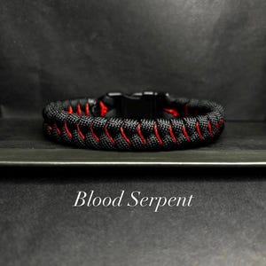 May include: A black and red paracord bracelet featuring a woven pattern with a black plastic side-release buckle. The text Blood Serpent is printed in white below the bracelet on a dark background.