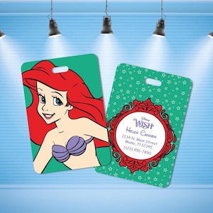 May include: Two rectangular luggage tags with rounded corners. One tag features a graphic of a red-haired mermaid with a purple shell top on a green background. The other tag has a green star pattern, a red ornate frame, and text reading Disney WISH, Helen Carson, 1234 N. Main Street, Miami, Fl 12345, (123) 456-7890.
