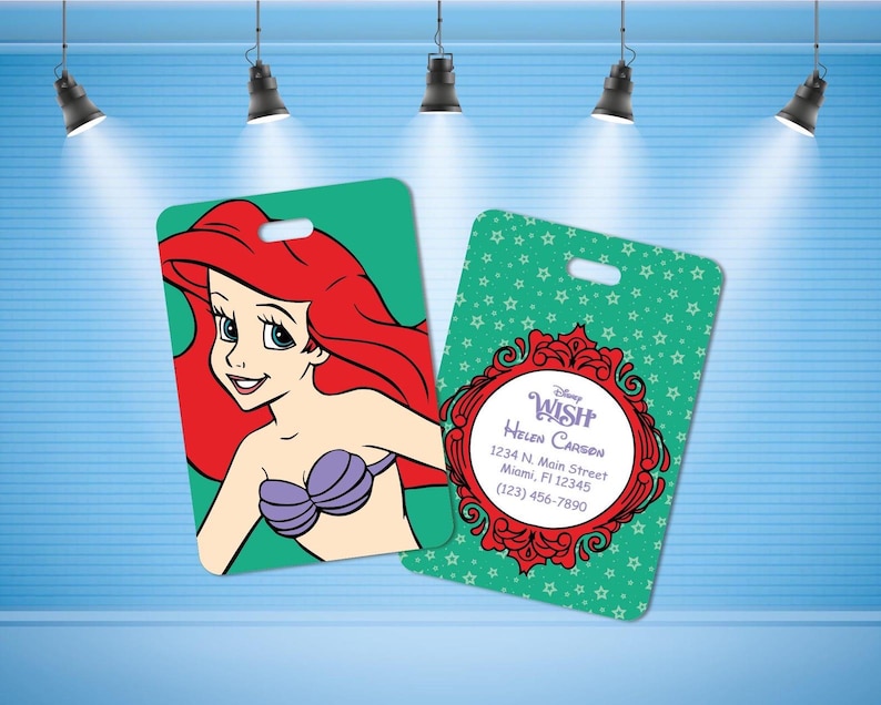 May include: Two rectangular luggage tags with rounded corners. One tag features a graphic of a red-haired mermaid with a purple shell top on a green background. The other tag has a green star pattern, a red ornate frame, and text reading Disney WISH, Helen Carson, 1234 N. Main Street, Miami, Fl 12345, (123) 456-7890.