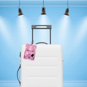 May include: A white hard-shell suitcase with a retractable handle and a pink luggage tag attached. The tag features a graphic of a pink cartoon character winking with the text "For Your Bag!" printed in white letters on the front surface.