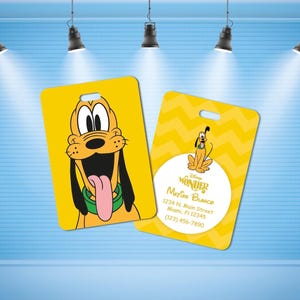May include: Two rectangular yellow luggage tags featuring Pluto. One tag shows a close-up of Pluto's face with a green collar. The other tag has a yellow chevron pattern, a small Pluto illustration, and the text Disney Wonder, Matías Blanco, 1234 N. Main Street, Miami, Fl 12345, (123) 456-7890.