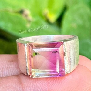 May include: A silver ring featuring a large, square-cut, multi-colored gemstone that transitions from yellow to pink and purple. The band is wide and smooth with a polished metallic finish. The text SilverCraftGift is visible above the ring.