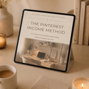 May include: A tablet showing "The Pinterest Income Method" with the text "Turn Simple Pins Into Daily Passive Sales Without Showing Your Face." The image includes a coffee mug, a notebook, a pen, and a lit candle.