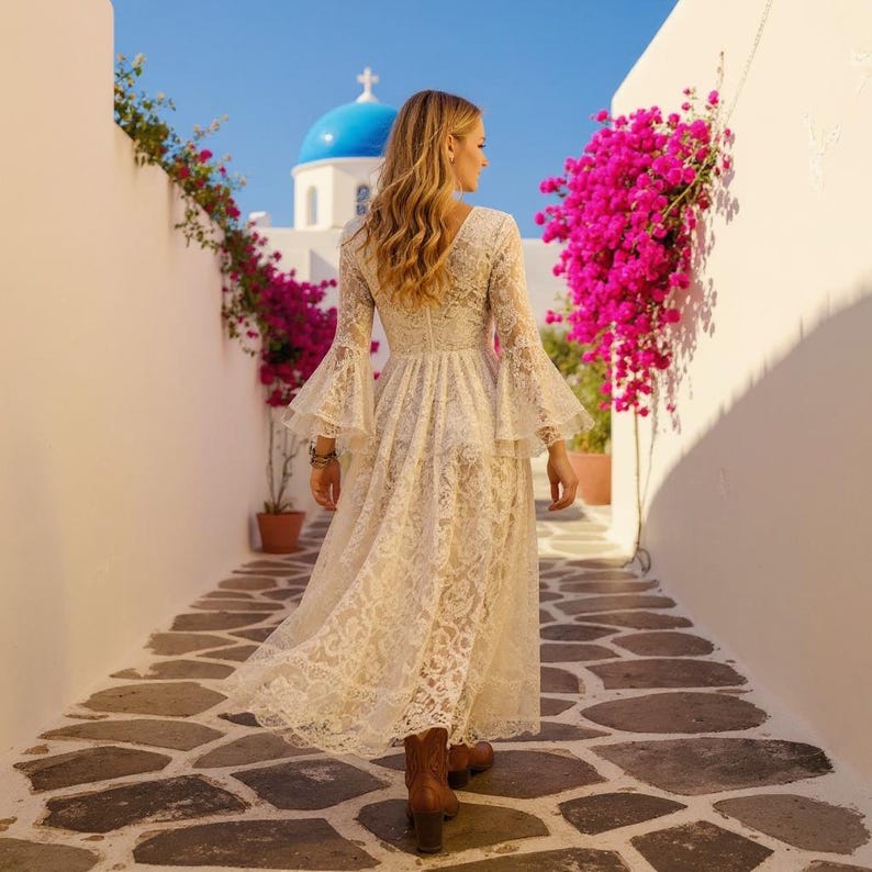 May include: A long, cream-colored lace dress featuring long, flared bell sleeves and a fitted bodice that flows into a full-length skirt. The garment is constructed from intricate floral lace fabric and is paired with brown leather ankle boots.