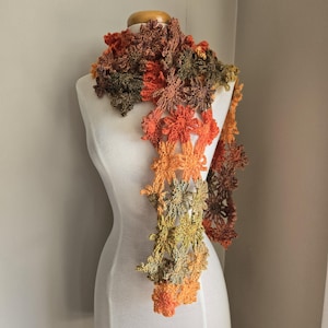 May include: A crocheted scarf with a floral design in shades of orange, brown, and green.