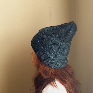 以下が含まれることがあります： 濃いティール色のニット帽。ケーブル編みの模様が施されています。帽子は柔らかい、おそらくウール素材で作られています。冬のアクセサリーです。