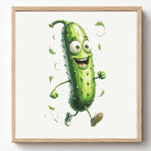 May include: A cross-stitch embroidery pattern featuring a bright green, anthropomorphic pickle character with large eyes and a wide, happy smile, depicted in a running motion with small green leaf accents, framed in a light-colored wooden square frame.