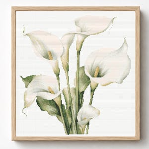 May include: A cross-stitch pattern featuring a bouquet of white calla lilies with yellow spadices and green stems and leaves, presented within a light-colored wooden square frame. The design uses a grid-like stitch technique on a white background.