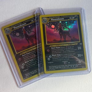 May include: Two Houndoom trading cards encased in clear plastic protective sleeves. Each card features a holographic illustration of the canine-like creature against a starry, colorful sky. The cards display the name Houndoom, 70 HP, and text.