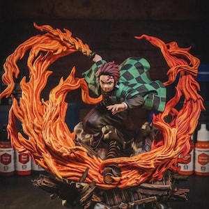 Könnte beinhalten: Eine detaillierte Anime-Charakterfigur, die eine Person mit burgunderrotem Haar und einem grün-schwarz karierten Haori zeigt, die ein Schwert schwingt, umgeben von großen, modellierten orangefarbenen und gelben Flammen auf einem Sockel aus Holztrümmern.