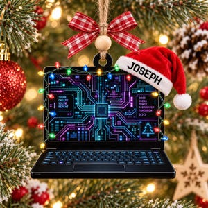 May include: A laptop-shaped ornament featuring a circuit board screen with the text 'THINK CREATE SOLVE REPEAT' and 'GOOD IDEAS POWER A BRIGHTER TOMORROW', wrapped in colorful string lights, topped with a red Santa hat labeled 'JOSEPH' and a red plaid bow.