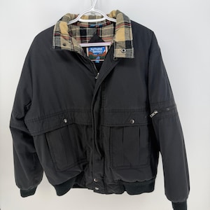 May include: Black bomber jacket with a plaid collar and the text "Northwest Territory". The jacket has two front pockets, two chest pockets, and a zippered pocket on the sleeve. The jacket has a ribbed knit hem and cuffs.