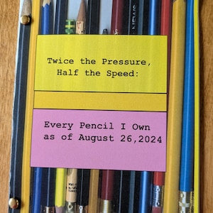 May include: A yellow notebook with a pink and yellow sticker that says "Twice the Pressure, Half the Speed: Every Pencil I Own as of August 26, 2024". The notebook has a photo of a collection of pencils on the front.