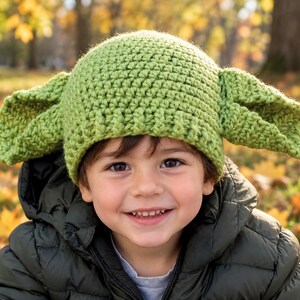 Puede incluir: Un gorro de ganchillo de color verde claro que presenta dos orejas grandes, puntiagudas y prominentes a los lados. El gorro está construido con un patrón de puntos texturizados y repetitivos, diseñado para cubrir la cabeza con un ajuste ceñido.