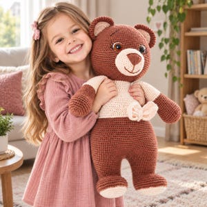May include: A large crocheted teddy bear featuring a dark brown head, arms, and legs, with a cream-colored chest and muzzle. The bear has dark brown stitched eyes, a dark brown nose, and a cream-colored bow attached to the center of its chest.