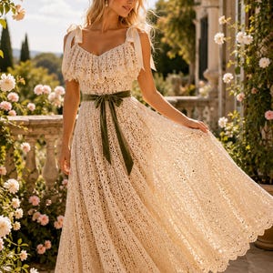 Può includere: Un abito midi in pizzo color crema con scollo a balze, spalline con fiocchi e un nastro di velluto verde oliva scuro legato in vita. L'abito presenta una gonna ampia e fluida con un orlo smerlato e intricati motivi floreali.