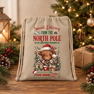 Può includere: Una borsa in tela beige con coulisse e il testo Special Delivery FROM THE NORTH POLE Do not open before December 25. La grafica mostra una mucca Highland con un cappello da Babbo Natale, una casetta, una tazza e un regalo. YOUR NAME è stampato sotto.