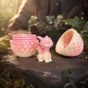 May include: A small, pearlescent pink and white dragon figurine standing next to an open, two-piece egg-shaped container. The container features a textured, scale-like exterior pattern and a smooth interior, with a threaded rim for closing.