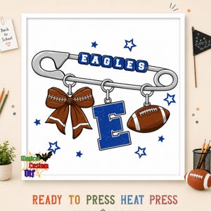 May include: A graphic design featuring a large silver safety pin with blue beads spelling EAGLES. Hanging from the pin are a brown cheer bow, a large blue letter E, and a brown football. The design includes blue stars on a white background.