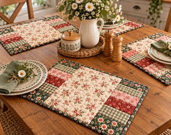 May include: Rectangular quilted placemats featuring a central cream panel with a small red and green floral print, bordered by patchwork strips of red floral, green gingham, and dark green daisy patterns, finished with a dark green binding edge.