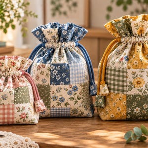 May include: Three drawstring pouches in small, medium, and large sizes, each featuring a patchwork design of floral and gingham patterns. The smallest pouch has pink accents, the medium has blue, and the largest has yellow and green tones.