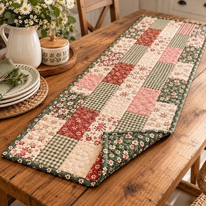 Könnte beinhalten: Ein rechteckiger, gesteppter Tischläufer mit einem Patchwork-Design aus abwechselnden Quadraten. Das Muster umfasst florale Drucke in Rot, Grün und Creme sowie grün-weiß karierte Stoffe und einfarbige, cremefarbene Quadrate mit Steppstruktur.