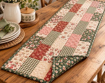 May include: A rectangular quilted table runner featuring a patchwork design of alternating squares. The pattern includes floral prints in red, green, and cream, alongside green and white gingham checks and solid cream squares with a stitched texture.