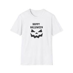 Puede incluir: Una camiseta blanca de manga corta con un estampado gráfico negro en el pecho. El diseño incluye el texto "HAPPY HALLOWEEN" en una fuente estilizada sobre una cara de calabaza geométrica con ojos triangulares y una boca dentada.