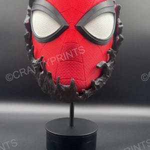 May include: A red textured mask with a black web pattern and large white mesh eye lenses, partially encased in a black, organic-looking substance. The mask is mounted on a black cylindrical stand. The text CRAFTYPRINTS is visible on the image.