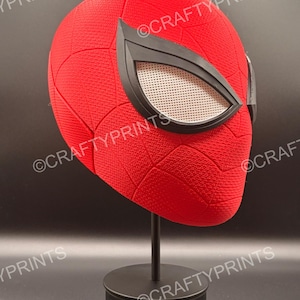 May include: A red full-head mask with a textured surface and a black web pattern. The mask features large, angular black-rimmed eye lenses with a white mesh screen. The mask is displayed on a black stand. The text CRAFTYPRINTS is visible.