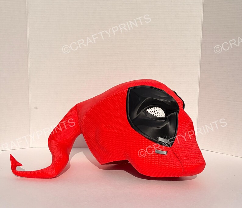 May include: A bright red textured mask featuring a long, curved tail-like extension, a black eye area with white mesh lenses, and two small silver-colored accents near the cheek. The text CRAFTYPRINTS is visible in the background.