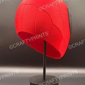May include: A bright red, textured, dome-shaped headpiece featuring a web-like pattern across its surface. The object is displayed on a black stand and includes the repeated watermark text CRAFTYPRINTS across the image.