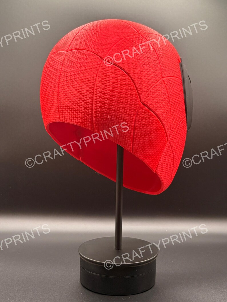 May include: A bright red, textured, dome-shaped headpiece featuring a web-like pattern across its surface. The object is displayed on a black stand and includes the repeated watermark text CRAFTYPRINTS across the image.