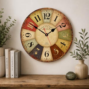 May include: A round wall clock with a distressed, multi-coloured segmented face featuring black Arabic numerals. The centre dial displays the text "CAFÉ de la TOUR" and "PARIS FRANCE" in black. It has two black hour and minute hands and a thin red second hand.
