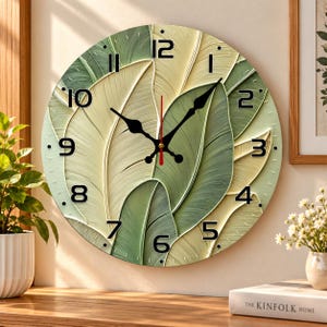 May include: A round wall clock featuring a textured surface of overlapping green and cream-colored leaves. The clock face displays bold black Arabic numerals from 1 to 12, with black hour and minute hands and a thin red second hand.