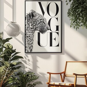 K&ouml;nnte beinhalten: Schwarz-wei&szlig; gerahmter Druck mit einem Leopardenprofil und dem Wort "VOGUE" in gro&szlig;en, schwarzen Buchstaben. Das Bild ist vor einem wei&szlig;en Hintergrund platziert, was einen starken Kontrast erzeugt. Der Druck wird in einem Raum mit Pflanzen und einem Holzstuhl ausgestellt.