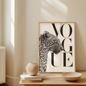 K&ouml;nnte beinhalten: Gerahmter Schwarz-Wei&szlig;-Druck mit dem Profil eines Leoparden und dem Wort "VOGUE" in gro&szlig;en Buchstaben. Das Kunstwerk h&auml;ngt an einer hellen Wand, mit einem Holztisch im Vordergrund mit einer Vase, B&uuml;chern und einer Schale.