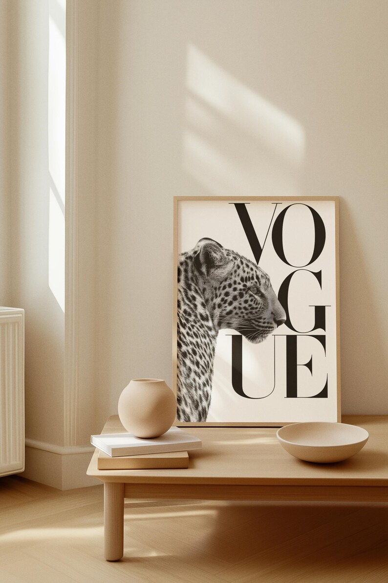 K&ouml;nnte beinhalten: Gerahmter Schwarz-Wei&szlig;-Druck mit dem Profil eines Leoparden und dem Wort "VOGUE" in gro&szlig;en Buchstaben. Das Kunstwerk h&auml;ngt an einer hellen Wand, mit einem Holztisch im Vordergrund mit einer Vase, B&uuml;chern und einer Schale.