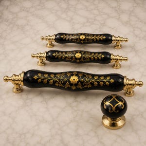 May include: Three black cabinet pulls and one matching round cabinet knob, all featuring a glossy finish with intricate gold floral patterns and polished gold-tone metal hardware at the ends and bases for a secure mounting installation.