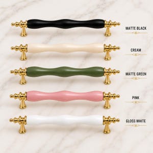 May include: Five cabinet pulls with gold-toned metal ends and central bars in matte black, cream, matte green, pink, and gloss white. Each pull features a wavy, contoured design with decorative finials and two mounting posts for installation.