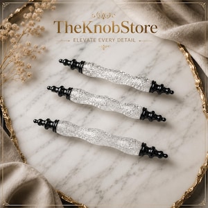 May include: Three cabinet pulls with clear, textured glass centers and black, tiered finial ends. The text TheKnobStore ELEVATE EVERY DETAIL is visible at the top. Each pull features a wavy, crystalline design with a reflective, crackled appearance.
