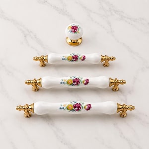 May include: A set of white ceramic cabinet hardware including one round knob and three drawer pulls of varying lengths. Each piece features a central floral pattern with red, yellow, and blue flowers and gold-toned metal end caps and bases.