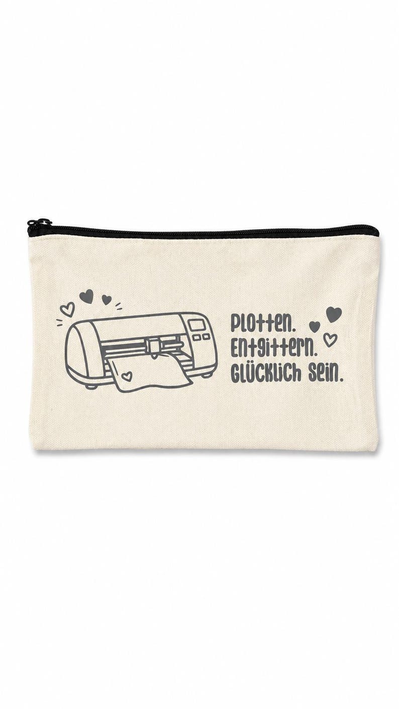 May include: A rectangular off-white canvas zipper pouch featuring a dark gray graphic of a cutting machine with hearts and the text "Plotten. Entgittern. GL&Uuml;CKLICH SEIN." printed in a dark gray sans-serif font on the front surface.