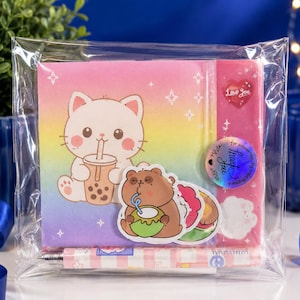 Peut inclure: Un carnet carré avec une couverture dégradée arc-en-ciel représentant un chat blanc buvant du thé boba, un ours brun buvant dans une noix de coco, un autocollant cœur rouge avec le texte Love You et un autocollant rond avec le texte Thank You.