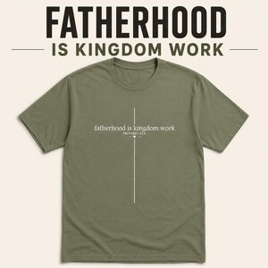 Könnte beinhalten: Ein olivgrünes T-Shirt mit dem Text "FATHERHOOD IS KINGDOM WORK" oben und "fatherhood is kingdom work" mit einem Kreuz-Design in der Mitte. Das Shirt hat einen Rundhalsausschnitt.