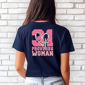 Puede incluir: Camiseta azul marino con un gráfico rosa en la espalda. El gráfico incluye el número 31, un corazón, una cruz y las palabras "PROVERBS WOMAN" en una fuente desgastada. La camiseta está hecha de un material suave.