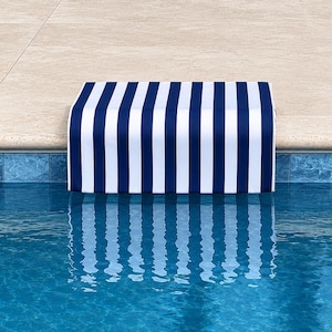 May include: A navy blue and white striped pool cover sits on the edge of a pool. The cover's reflection is visible in the clear, blue water. The pool's edge is a light beige colour.