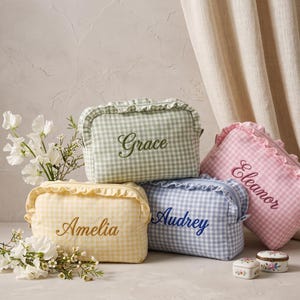 May include: Four rectangular zipped pouches with ruffled edges and a gingham pattern in sage green, soft pink, pale yellow, and light blue. Each pouch features a name embroidered in cursive script: Grace, Eleanor, Amelia, and Audrey.