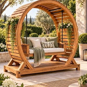 Puede incluir: Un banco columpio circular de madera con estructura de listones, asiento acolchado color crema y jardineras integradas con flores blancas y vegetación colgante. Incluye cojines de color verde oliva y estampados, además de una manta verde.